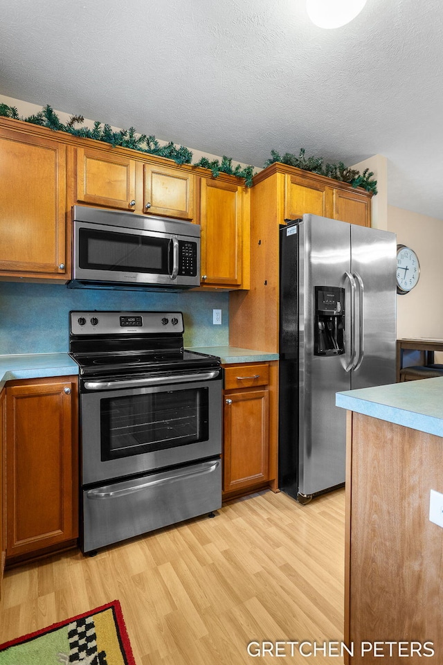 kitchen featuring stainless steel appliances, brown cabinetry, and light wood-style flooring