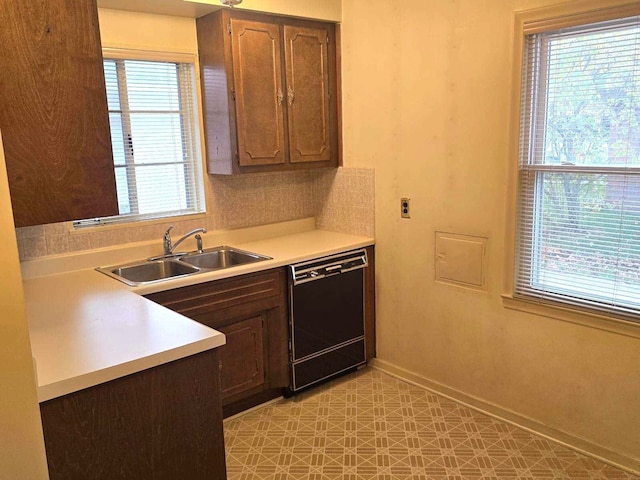 kitchen featuring light floors, light countertops, a sink, dishwasher, and baseboards