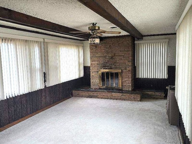 unfurnished living room with carpet, a fireplace, a ceiling fan, a textured ceiling, and beamed ceiling