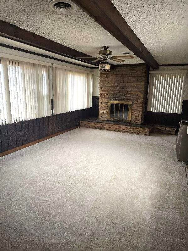 unfurnished living room with visible vents, a textured ceiling, carpet floors, a fireplace, and beam ceiling