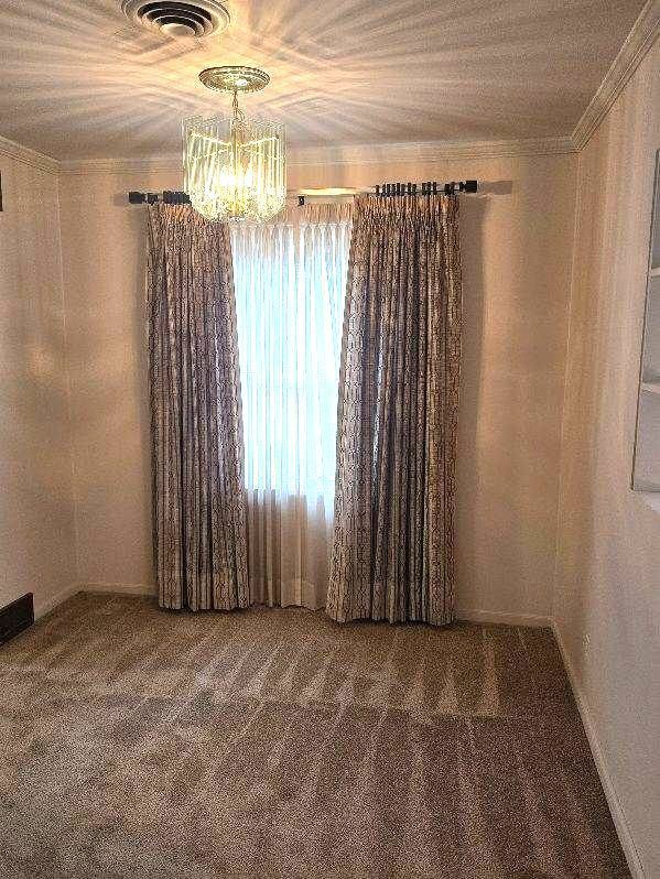 empty room with carpet, visible vents, a notable chandelier, and ornamental molding