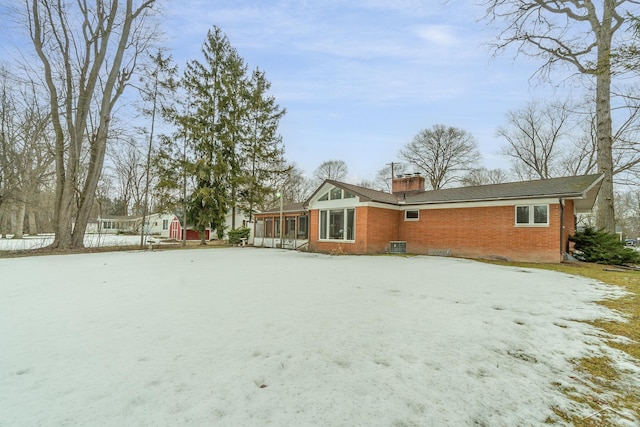 snow covered property featuring brick siding, a chimney, and a sunroom