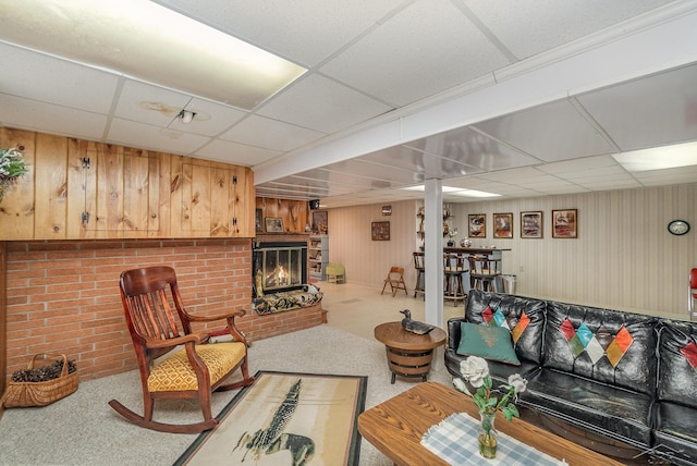 living area featuring carpet floors, a fireplace, a paneled ceiling, and wooden walls