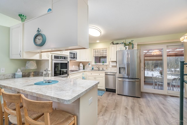 kitchen with light wood finished floors, light countertops, appliances with stainless steel finishes, a sink, and a peninsula