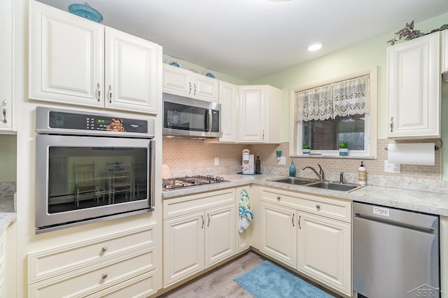 kitchen with light countertops, decorative backsplash, appliances with stainless steel finishes, a sink, and light wood-type flooring