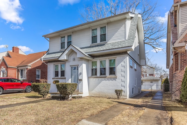 view of front of house with a front yard, roof with shingles, a detached garage, and brick siding