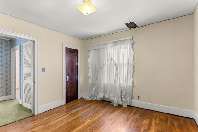 empty room featuring wallpapered walls, wood-type flooring, and baseboards