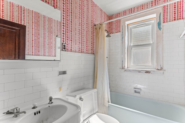 full bathroom with toilet, tile walls, wainscoting, shower / bath combo with shower curtain, and wallpapered walls