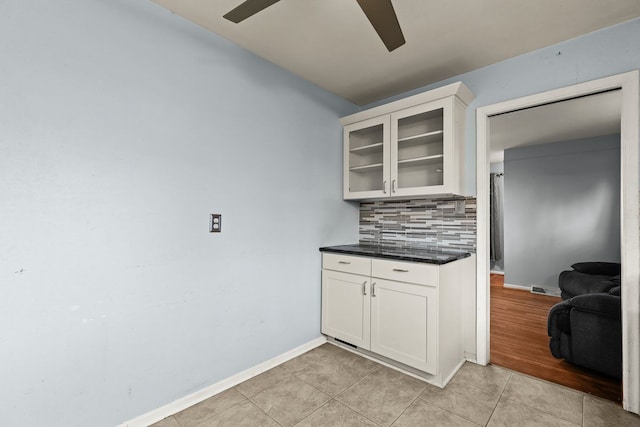 kitchen featuring ceiling fan, white cabinets, decorative backsplash, dark countertops, and glass insert cabinets