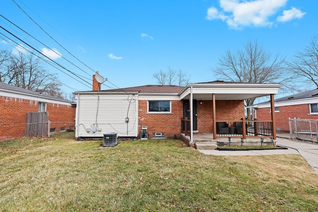 back of house featuring covered porch, brick siding, fence, a lawn, and a chimney