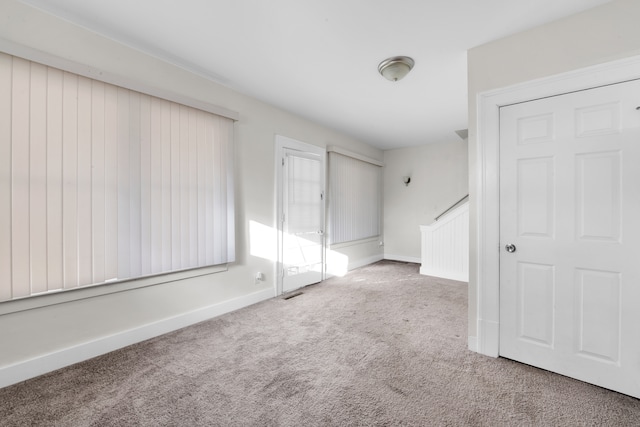 spare room featuring carpet floors, visible vents, baseboards, and stairs