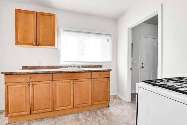 kitchen with a sink, baseboards, white gas range oven, brown cabinetry, and dark countertops