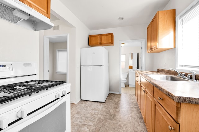 kitchen with a healthy amount of sunlight, white appliances, under cabinet range hood, and a sink