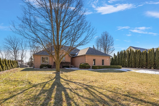 view of side of property featuring brick siding, a lawn, and fence