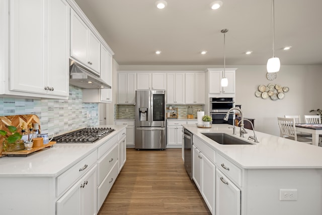 kitchen featuring a sink, under cabinet range hood, white cabinets, stainless steel appliances, and a kitchen island with sink