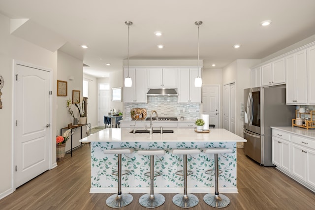 kitchen featuring a breakfast bar, wood finished floors, under cabinet range hood, and stainless steel appliances