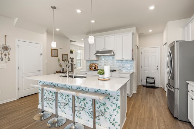 kitchen featuring a sink, under cabinet range hood, wood finished floors, freestanding refrigerator, and decorative backsplash