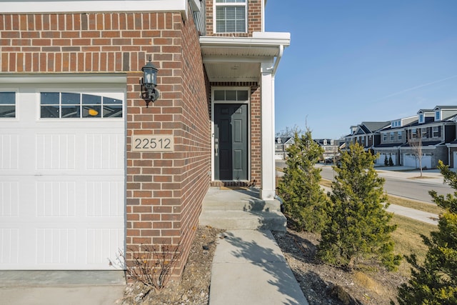 property entrance featuring a residential view, brick siding, and an attached garage