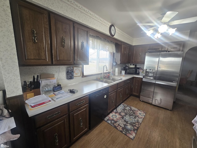 kitchen featuring wood finished floors, a sink, light countertops, black appliances, and wallpapered walls