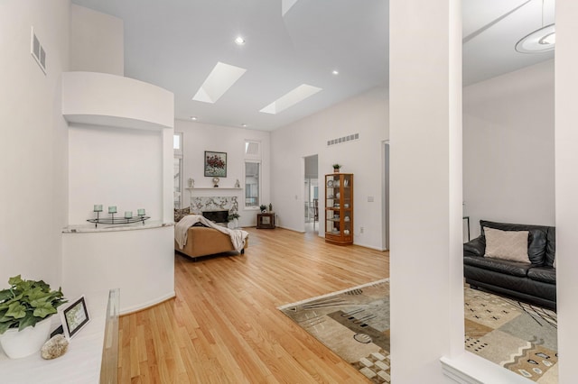 interior space featuring light wood finished floors, a skylight, a towering ceiling, and visible vents