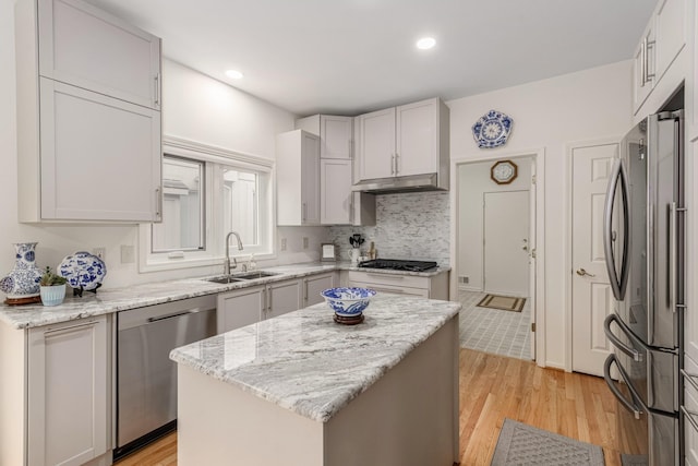 kitchen featuring appliances with stainless steel finishes, light wood-style floors, a sink, a kitchen island, and light stone countertops