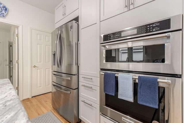 kitchen with stainless steel appliances, white cabinetry, and light wood finished floors