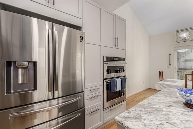 kitchen featuring baseboards, appliances with stainless steel finishes, light stone counters, vaulted ceiling, and light wood-style floors