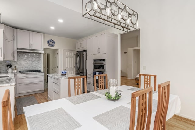 kitchen featuring light stone counters, a kitchen island, light wood-style floors, appliances with stainless steel finishes, and tasteful backsplash