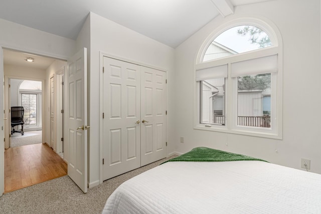 bedroom with lofted ceiling with beams, a closet, and light colored carpet