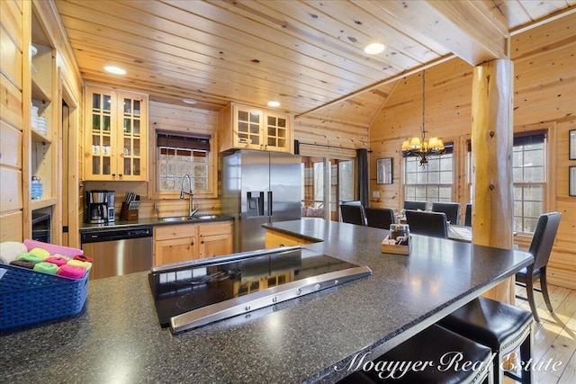 kitchen featuring dark countertops, appliances with stainless steel finishes, vaulted ceiling, a sink, and wood walls