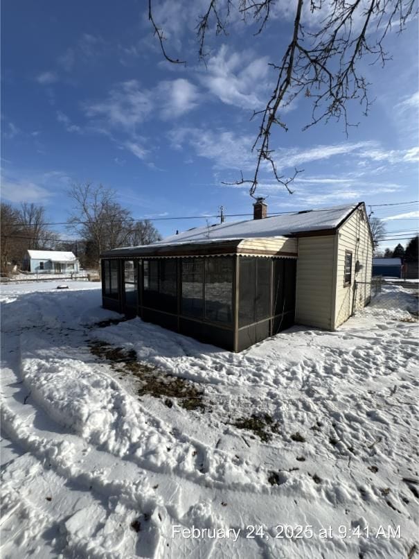 snow covered rear of property with a sunroom