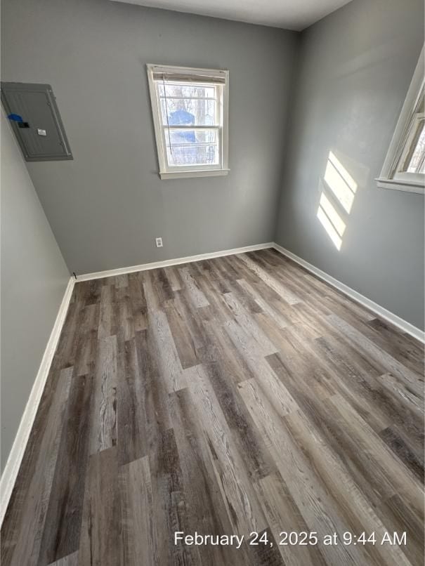 empty room featuring electric panel, baseboards, and wood finished floors