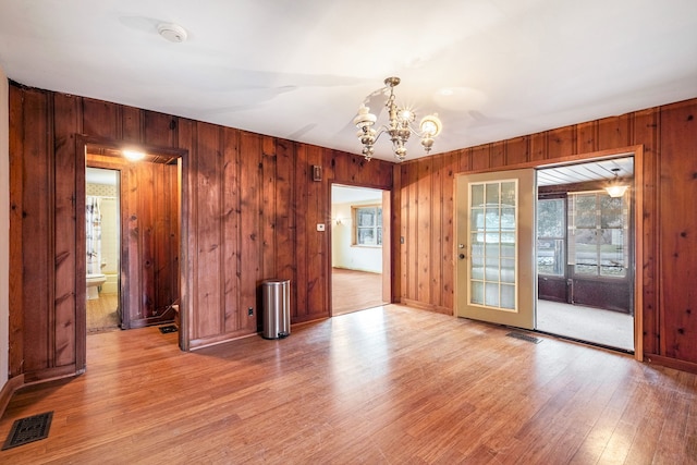 spare room featuring wood walls, light wood-type flooring, visible vents, and a notable chandelier