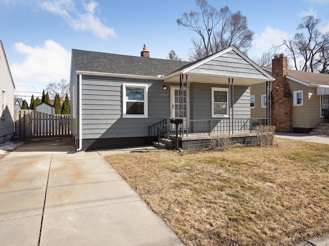 bungalow featuring a porch, a chimney, roof with shingles, and a front yard