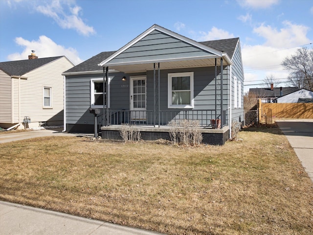 view of front facade featuring covered porch, a shingled roof, a front lawn, and fence