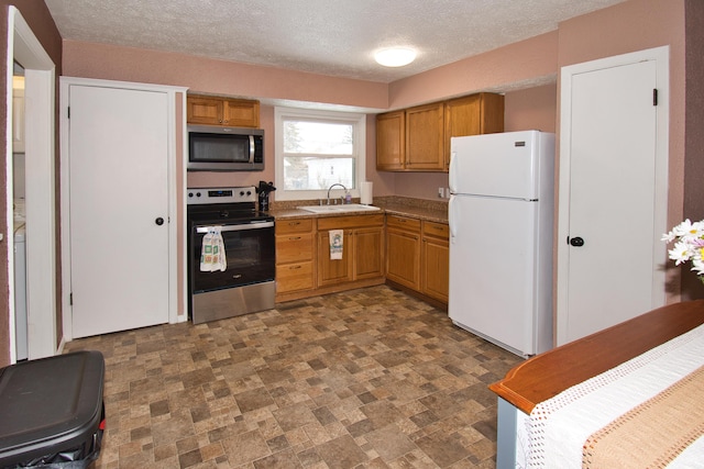 kitchen featuring brown cabinets, stainless steel appliances, stone finish floor, a sink, and a textured ceiling