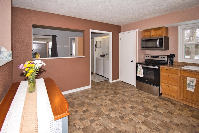 kitchen featuring baseboards, stone finish floor, appliances with stainless steel finishes, washing machine and clothes dryer, and a textured ceiling