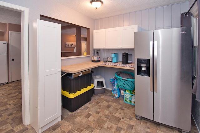 kitchen with white cabinets, stainless steel fridge with ice dispenser, stone finish floor, freestanding refrigerator, and light countertops