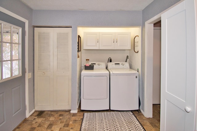 laundry area with cabinet space, washing machine and dryer, a textured wall, and stone finish flooring