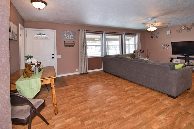 living room featuring light wood-style floors, ceiling fan, a textured ceiling, and baseboards