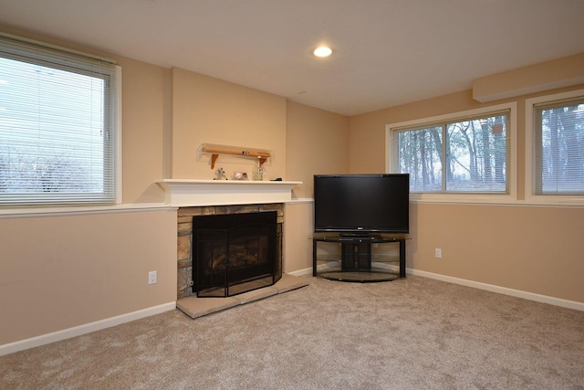 unfurnished living room featuring carpet, plenty of natural light, a stone fireplace, and baseboards