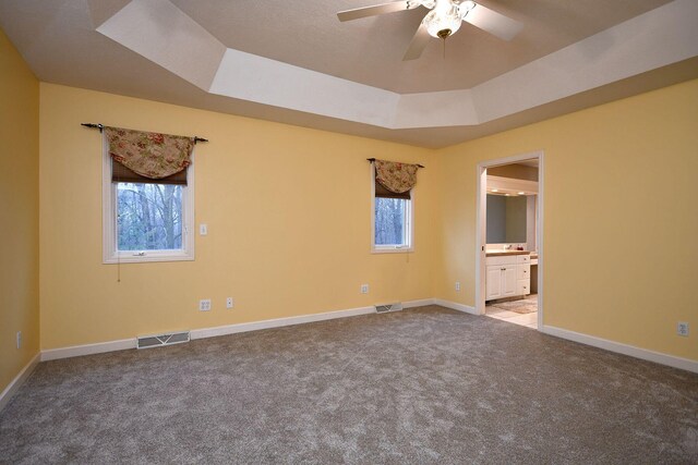 carpeted spare room with a ceiling fan, baseboards, visible vents, and a tray ceiling