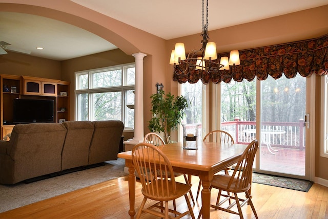 dining area featuring arched walkways, decorative columns, light wood finished floors, and an inviting chandelier