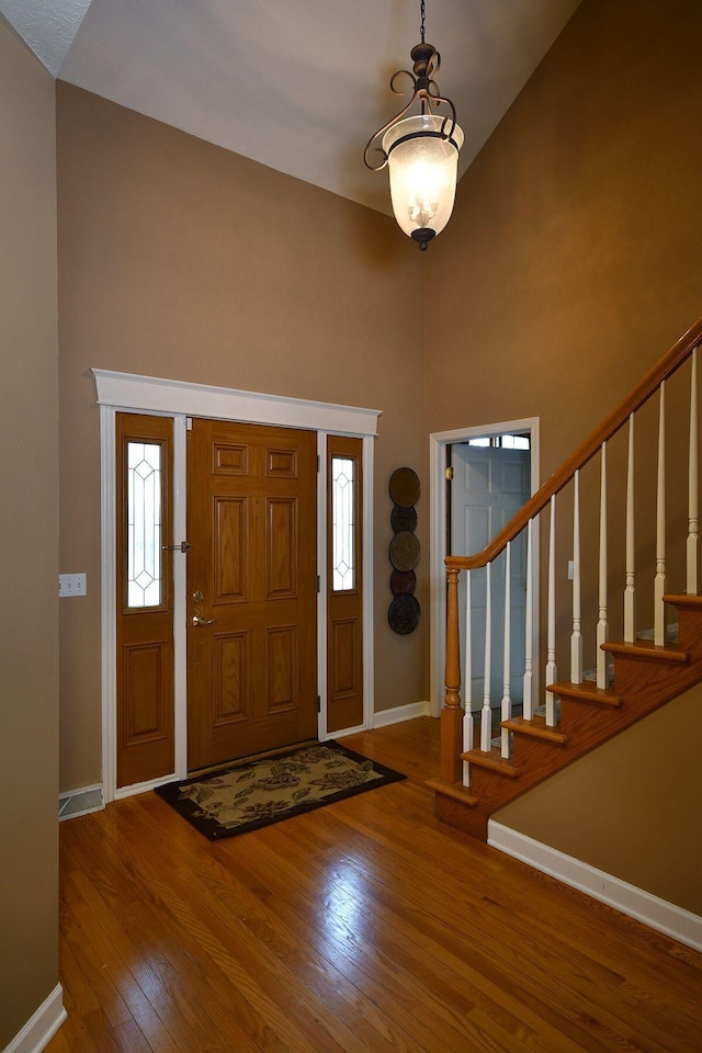 entryway with a towering ceiling, stairway, wood-type flooring, and baseboards