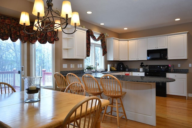 kitchen with open shelves, a breakfast bar, white cabinetry, black appliances, and light wood finished floors