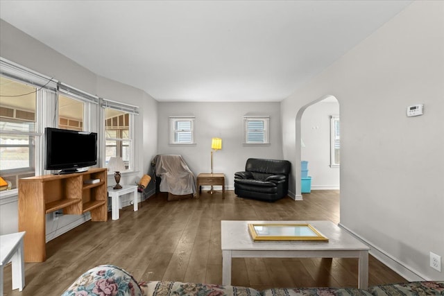 living area featuring arched walkways, wood finished floors, and baseboards