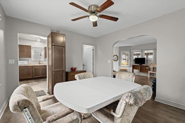 dining area with arched walkways, ceiling fan, wood finished floors, visible vents, and baseboards