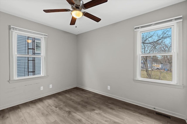 empty room with a ceiling fan, visible vents, baseboards, and wood finished floors