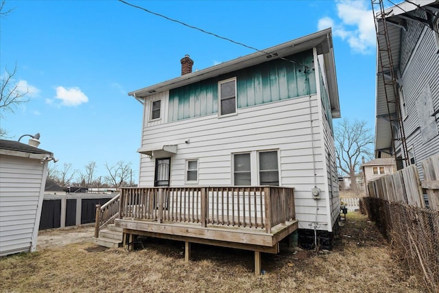 rear view of house with a deck, board and batten siding, a chimney, and fence