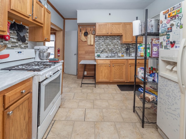 kitchen with white appliances, ornamental molding, a sink, light countertops, and backsplash